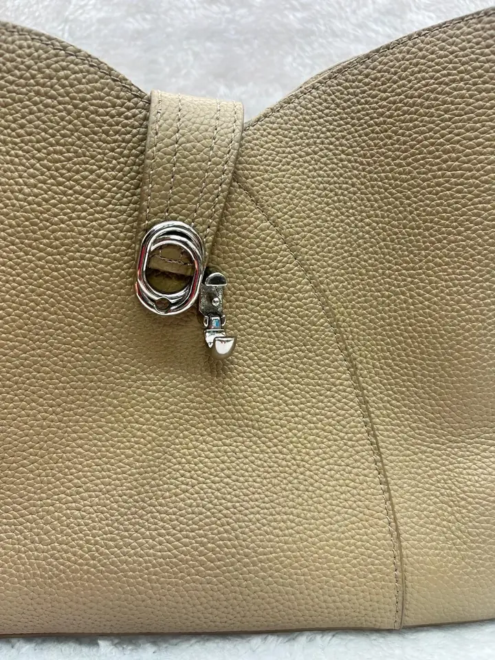 Close up showing the metal twist-lock closure on the beige pebbled leather cross body hand bag.