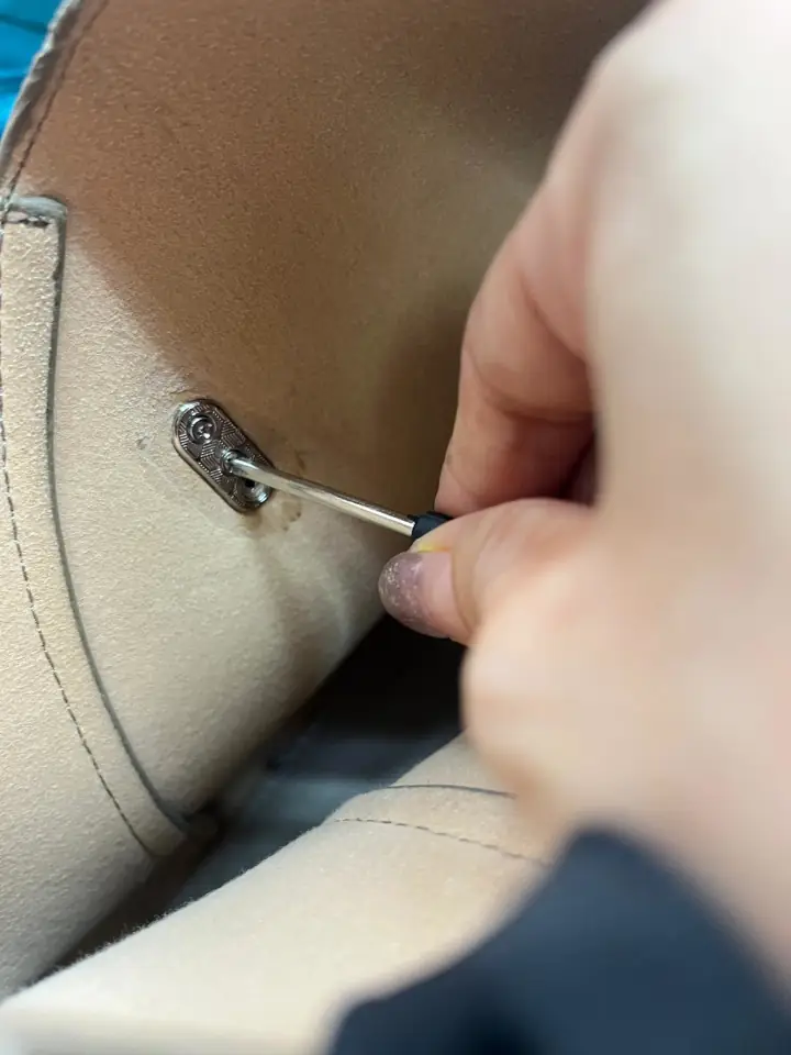 Unscrew the internal screws of the twist closure on the body of the beige leather handbag.
