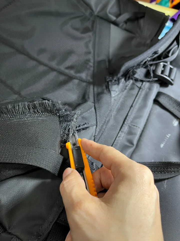 Using a penknife to remove the stitches from the North Face backpack to begin sewing the shoulder straps.