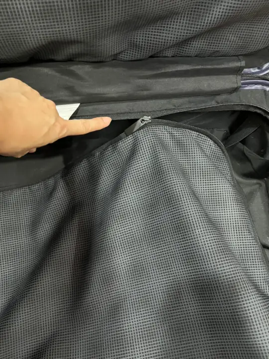 A finger pointing at the split zipper inside the black color luggage zipper compartment.
