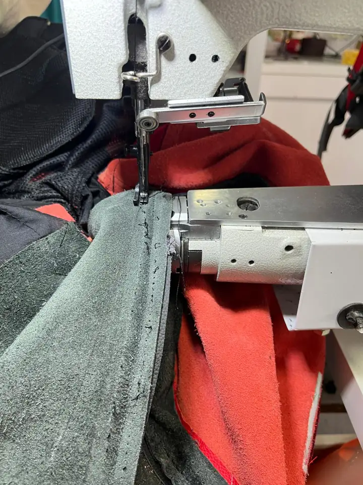 Red Ducati motorcycle jacket on a sewing machine, undergoing fitting alteration with focus on maintaining quality and design.